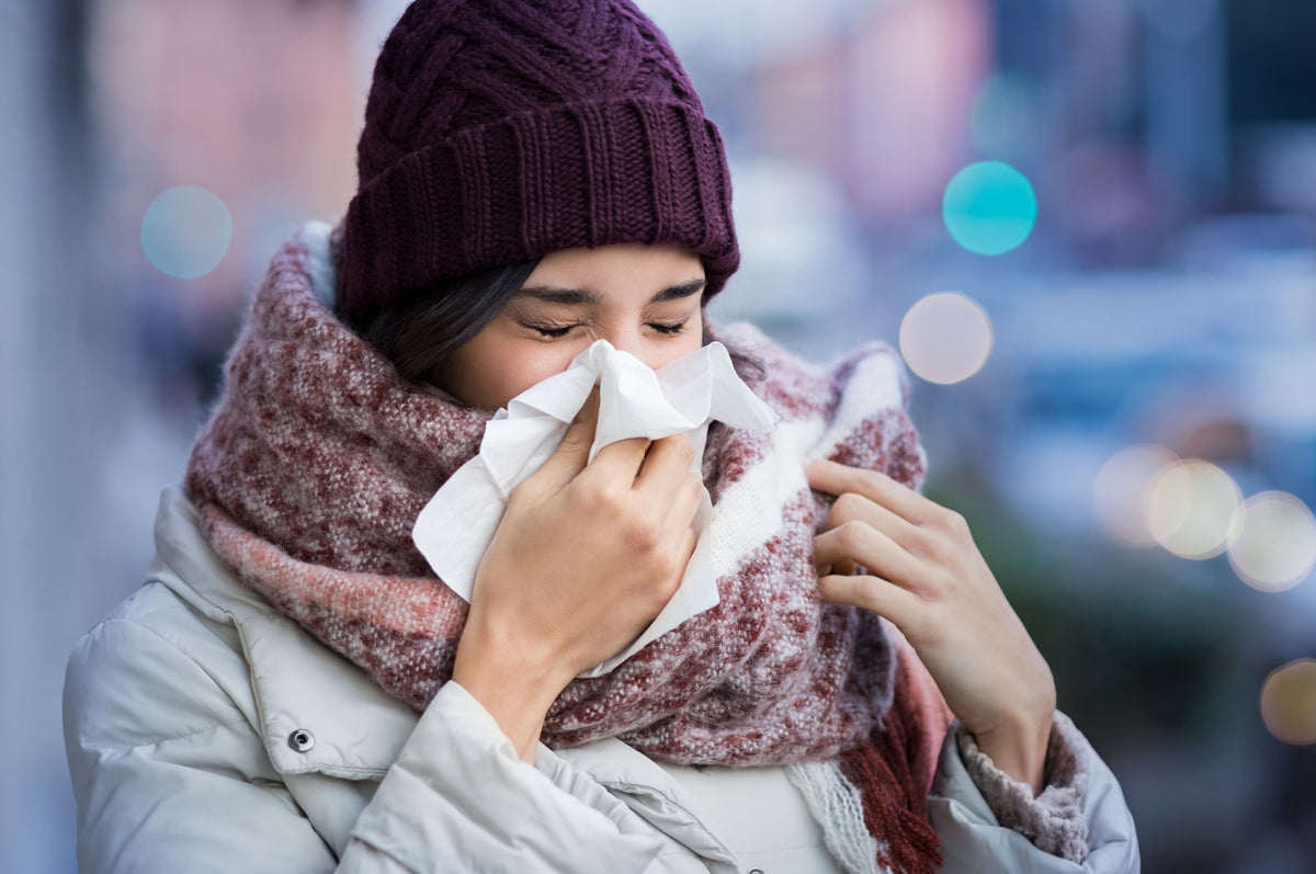 Eine Frau mit Winterjacke, Mütze und dickem Schal schneuzt sich die Nase